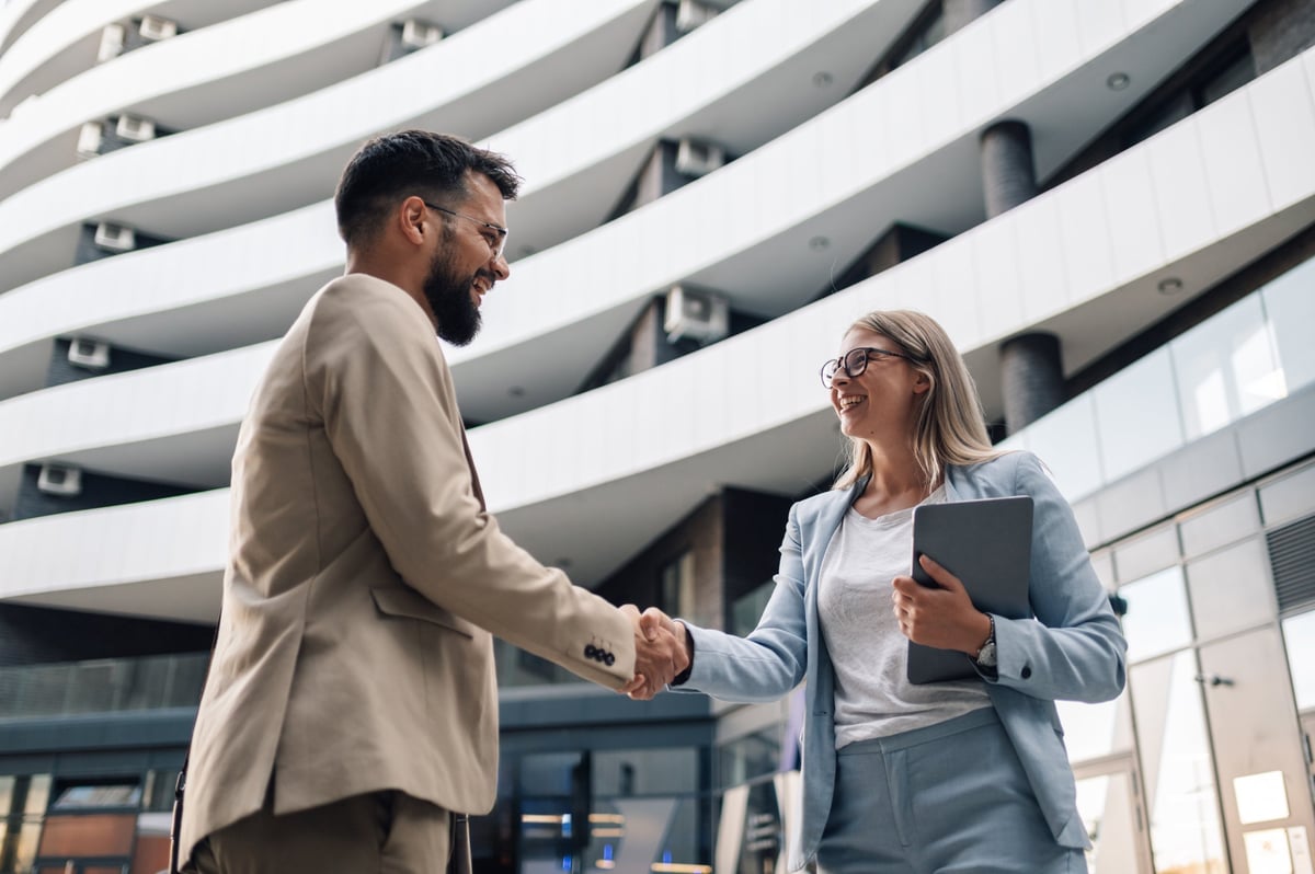 Two business partners happily shaking hands in front of office building